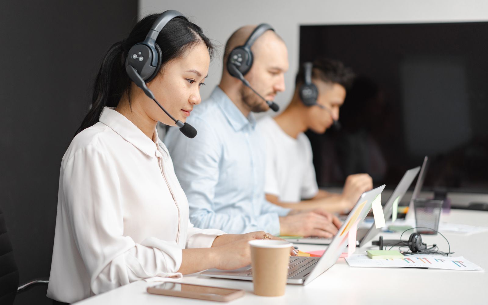 Equipo de agentes de soporte técnico con auriculares atendiendo a clientes en un service desk.